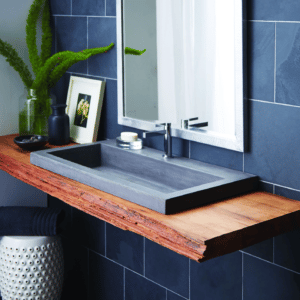 Rectangular gray concrete vessel sink on a live-edge wood floating vanity with a chrome faucet against a dark blue tile wall.