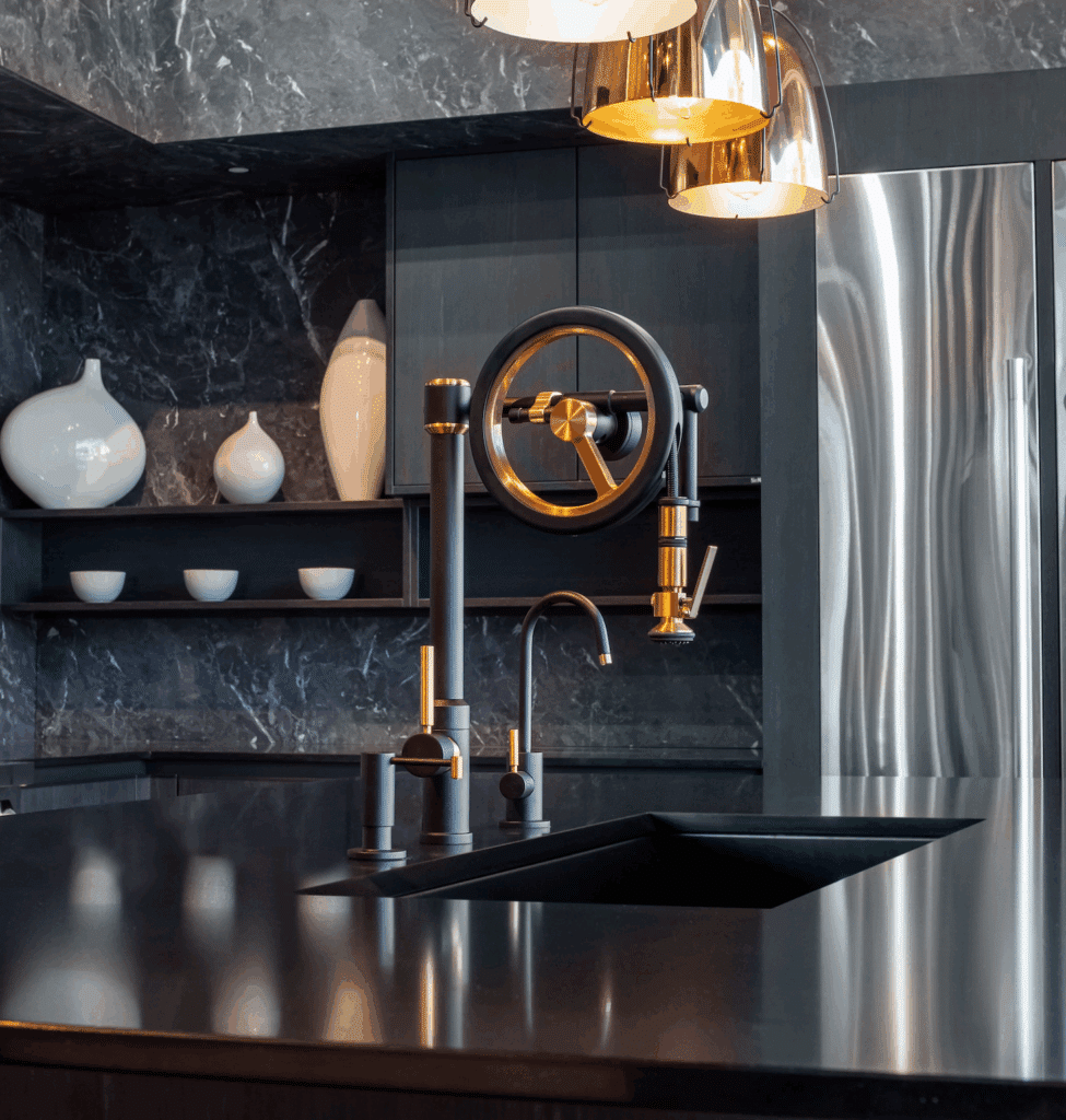 An industrial-style kitchen faucet in matte black and gold, featuring a prominent wheel handle, in a modern dark-toned kitchen.