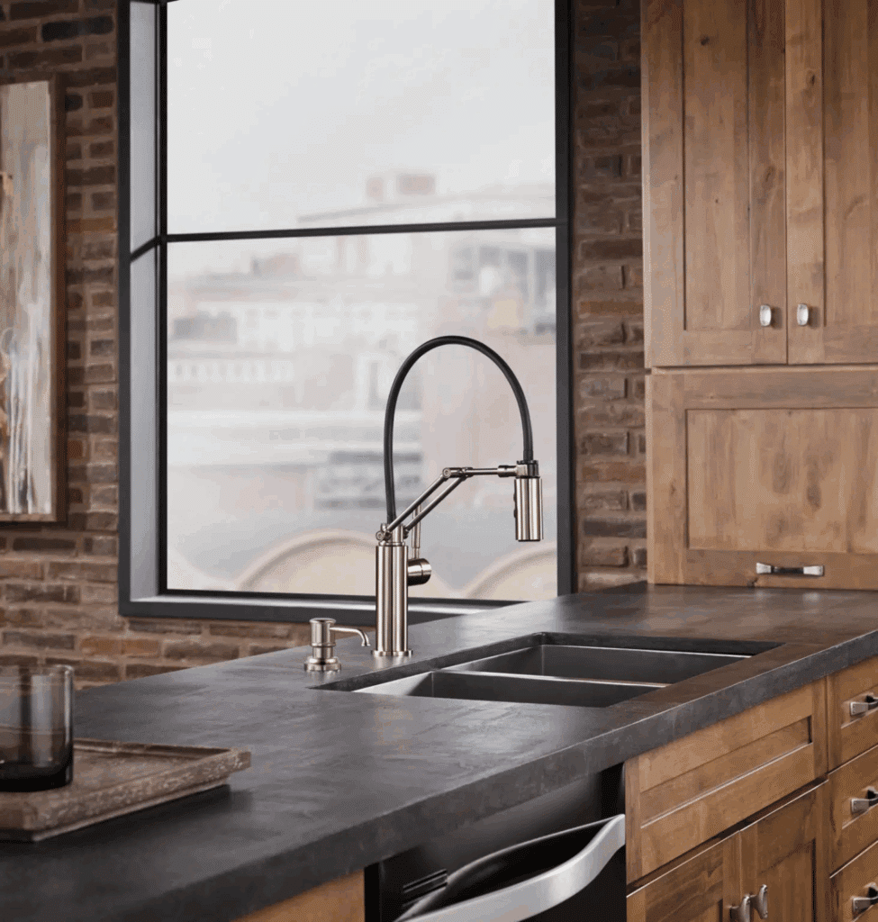 A modern, articulating spring-neck faucet in polished nickel, installed on a dark countertop with a double sink.