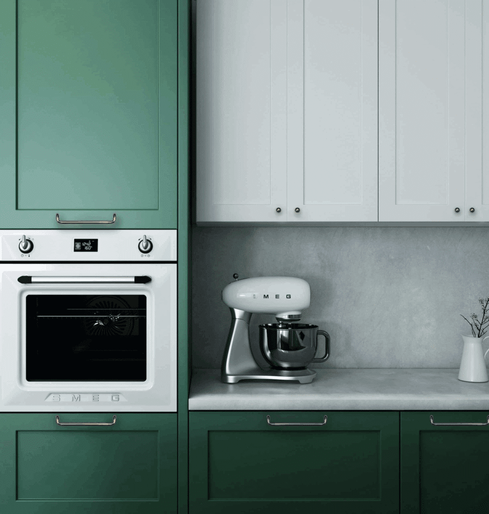 A modern kitchen with matte green and white cabinets with minimalistic cabinet hardware, a white Smeg wall oven, and a white Smeg stand mixer on a grey counter.